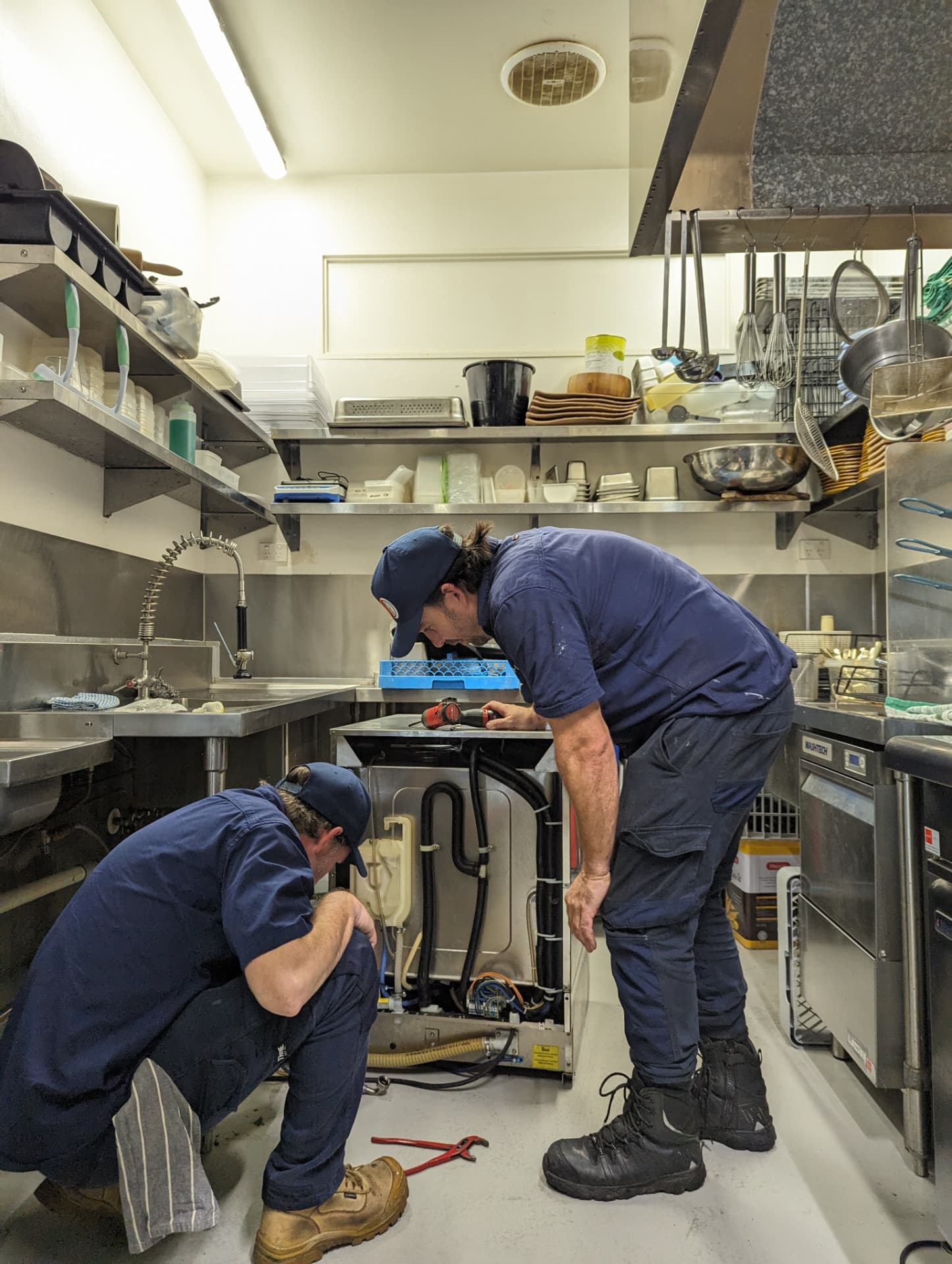 Two CHEFTECH technicians diagnosing a commercial underbench dishwasher on site