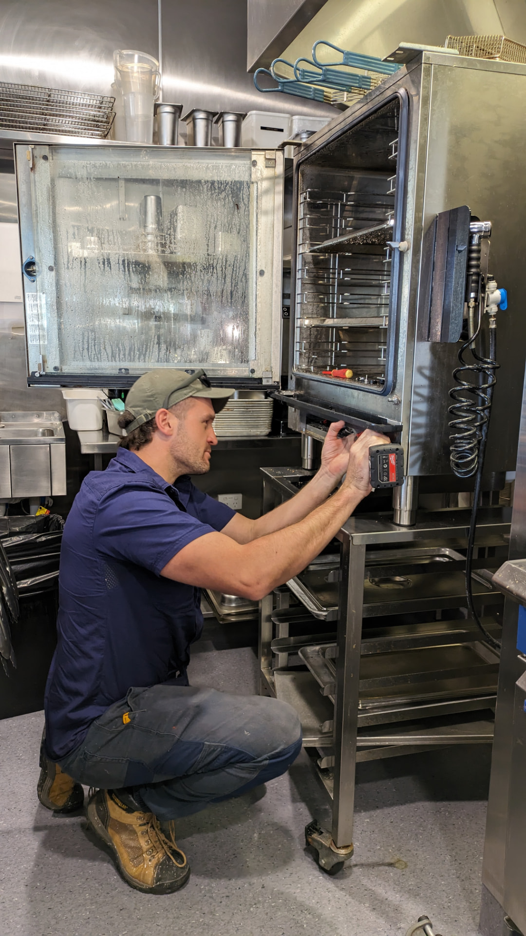 CHEFTECH technician servicing a commercial combi oven door and control panel in a working kitchen